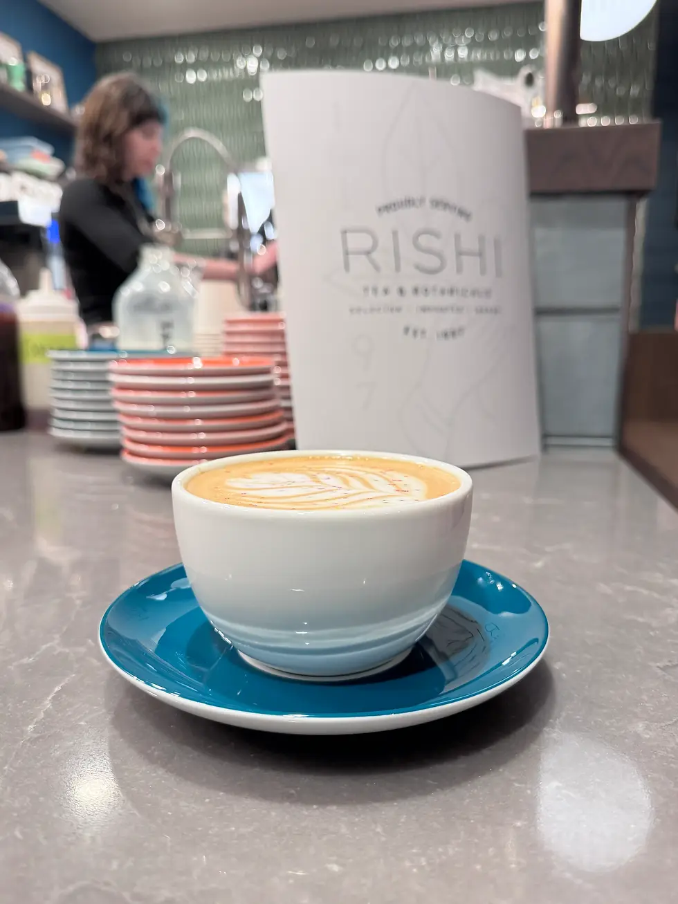 Beautifully crafted latte with latte art at a specialty coffee shop in Minneapolis-St.Paul, Minnesota. A cozy café ambiance featuring Rishi Tea menu and vibrant dishware in the background.