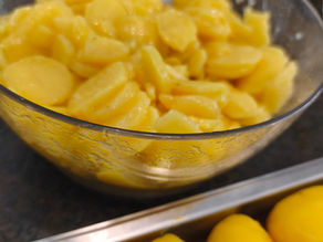 Schüssel mit Kartoffelsalat, daneben ganze Kartoffeln auf einem Blech in der Küche.