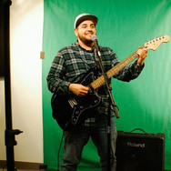 Joel playing guitar in front of a green screen.