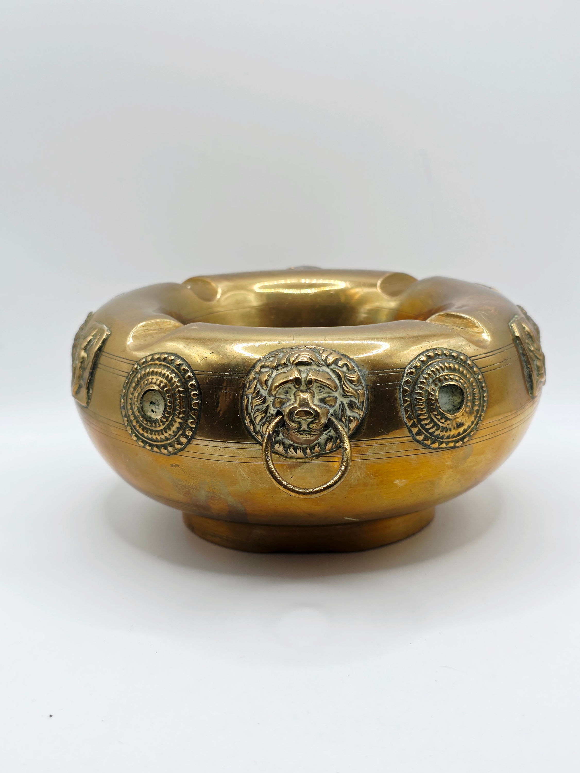 Side view of heavy mid century brass ashtray highlighting cast lion head ring handle attachment.