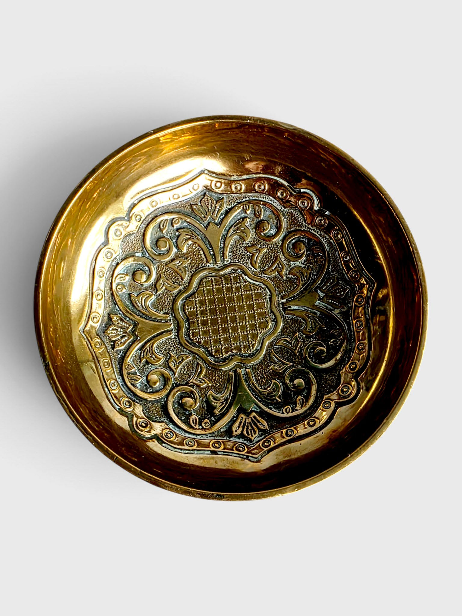 Top-down view of embossed foliate scrollwork inside mid-century Indo-Persian brass dish