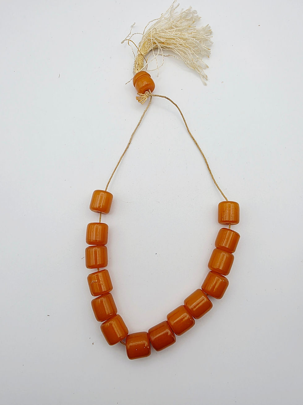 Full layout of a vintage amber butterscotch Bakelite prayer worry bead strand with tassel on a white background.