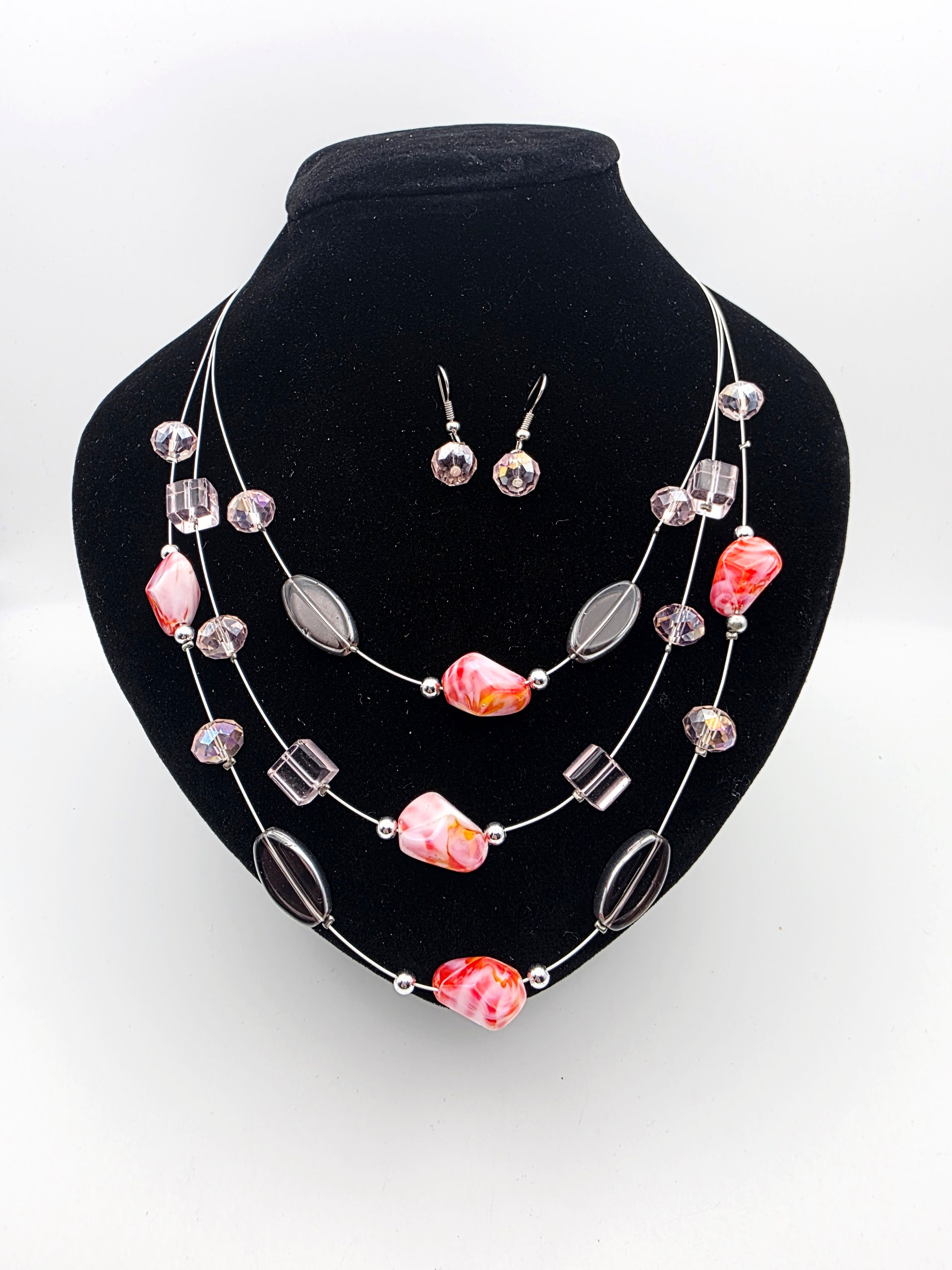 Overview layout of a pink multi strand floating wire necklace and drop earrings set on a black bust.