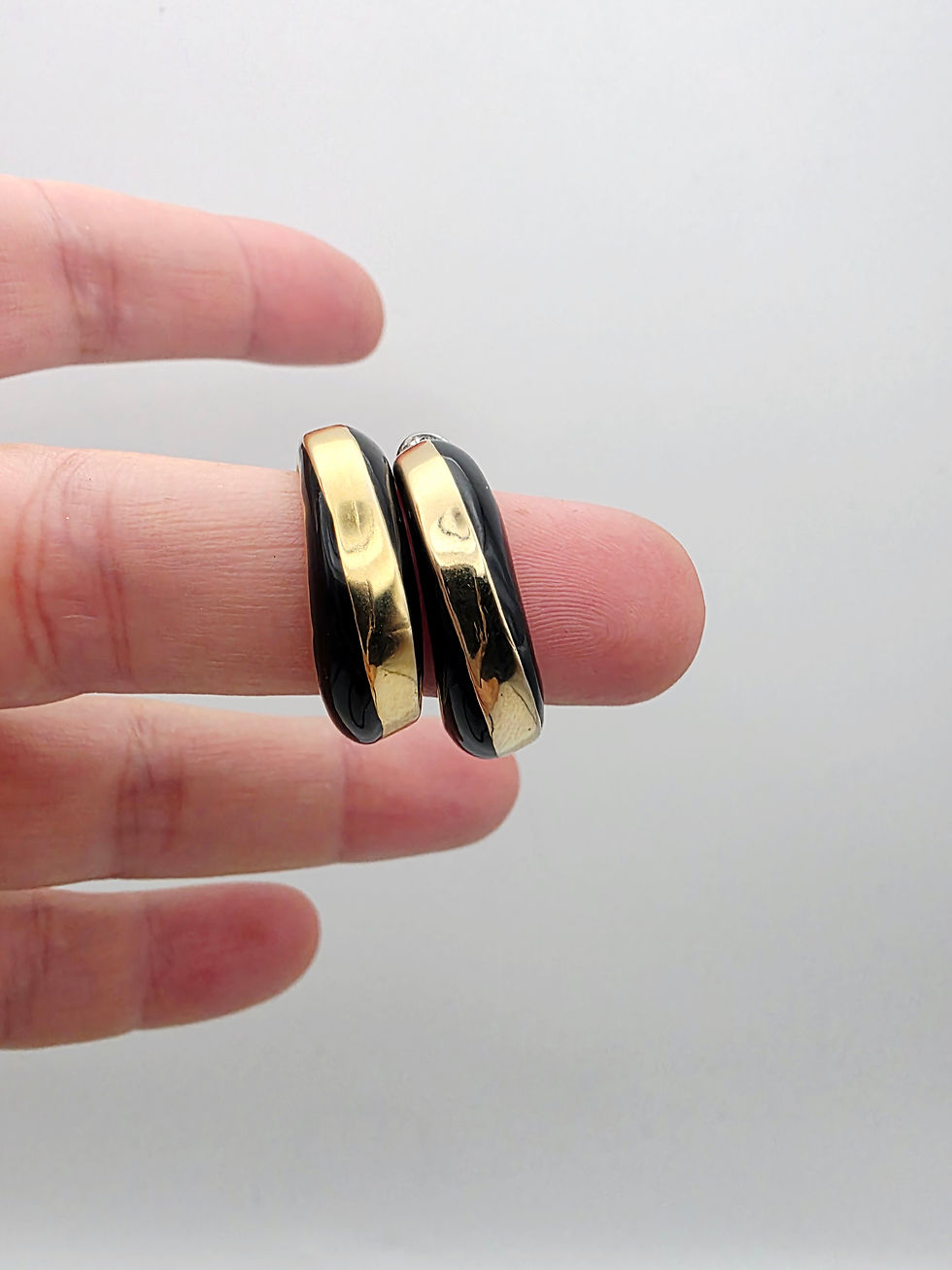 Handheld close-up showing two gold-tone metal hoop earrings with black enamel stripe inlay.