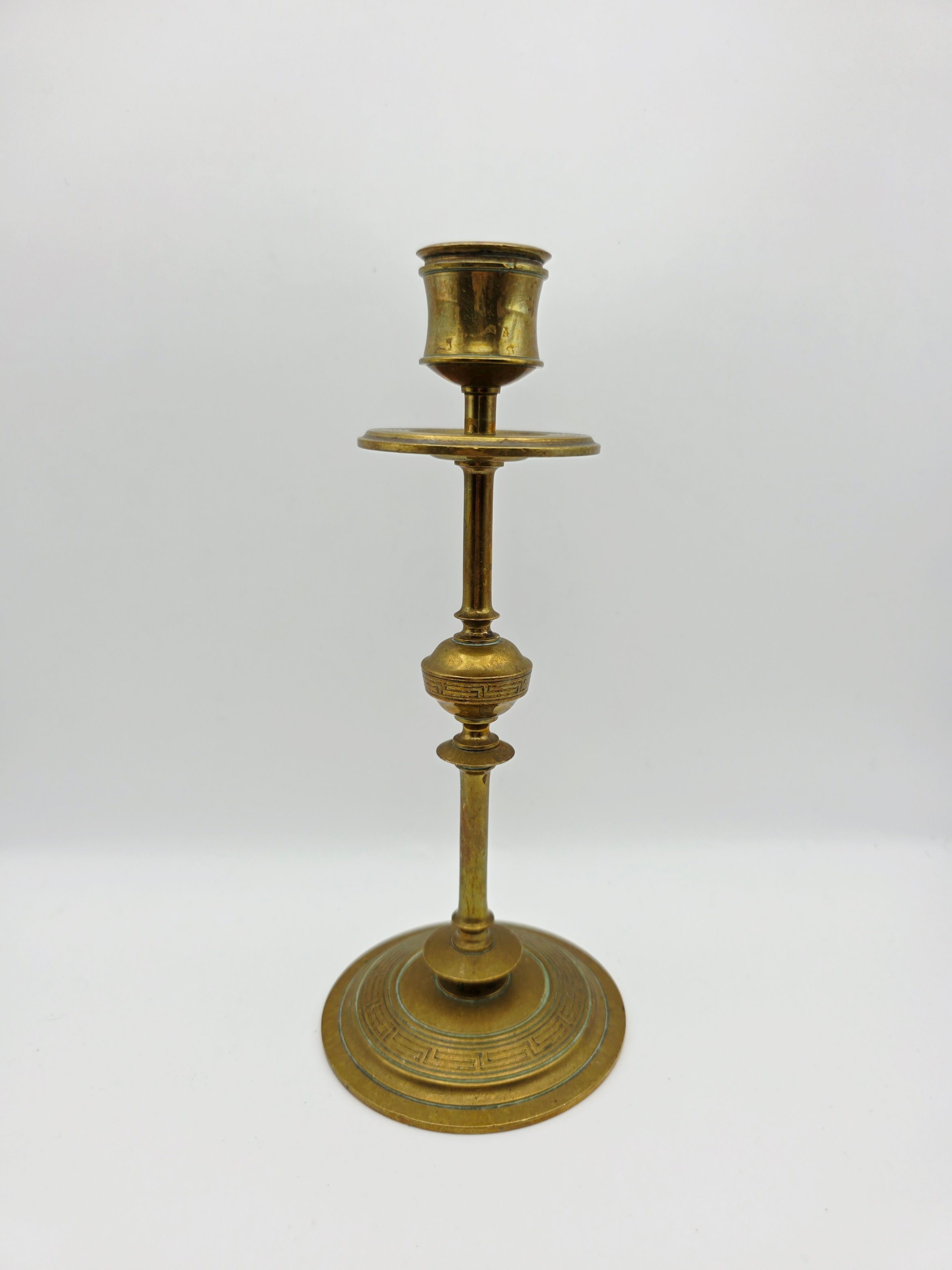 Mid-century brass taper candlestick with Greek Key motif on stepped base against white background