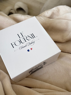 White Le Fournil pastry box resting on a beige blanket — the perfect setup for a cozy morning in.