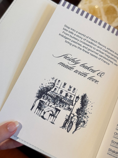 A close-up of Le Fournil’s illustrated menu featuring the tagline “Freshly baked & made with love."