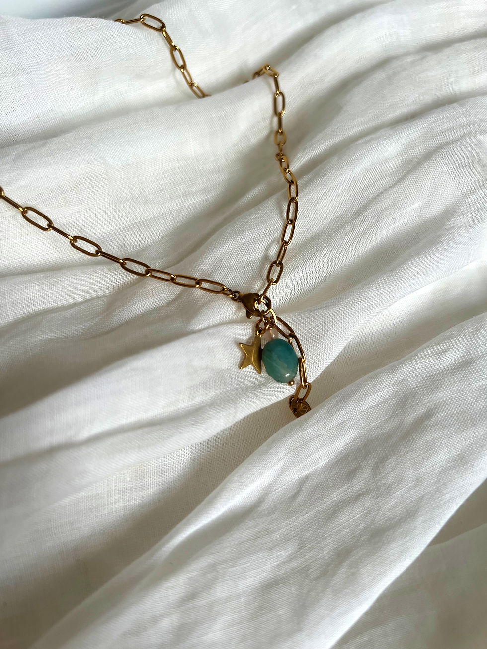 Goldene Kette mit Sternanhänger und blauem Stein auf weißem Stoff.