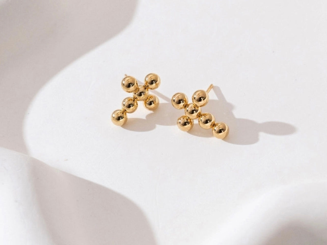 Goldene Kreuzohrringe, Nahaufnahme auf weißem Hintergrund, Schmuck Accessoire, schlichtes Design.