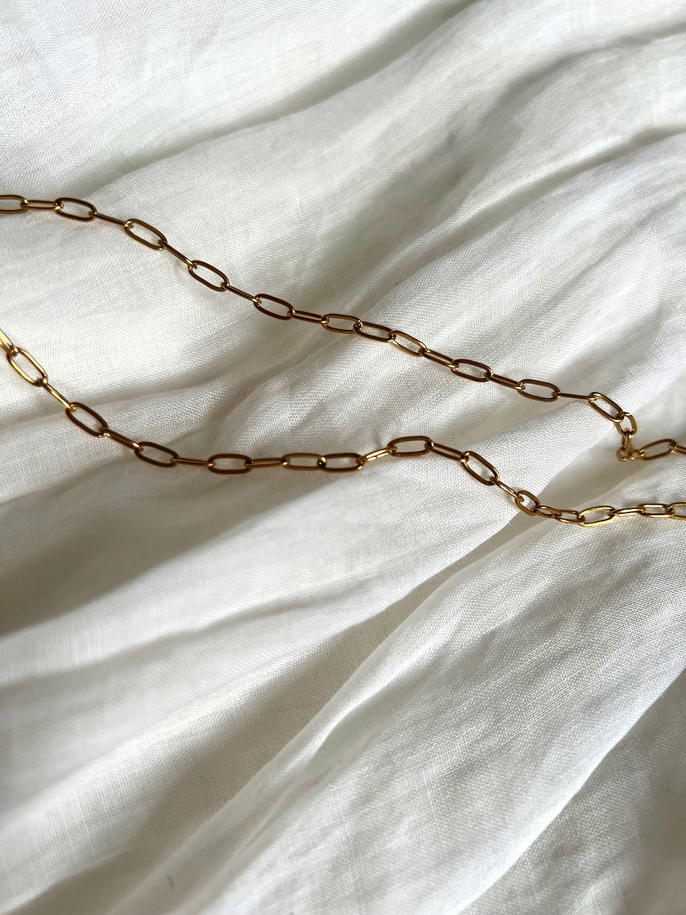 Goldene Halskette auf weißem Stoff, Schmuckstück und Modeaccessoire stilvoll präsentiert.