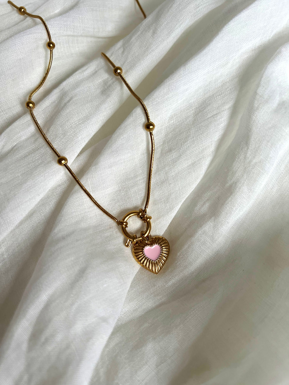 Goldene Halskette mit Herzanhänger auf weißem Stoff, Schmuckaccessoire, Nahaufnahme.