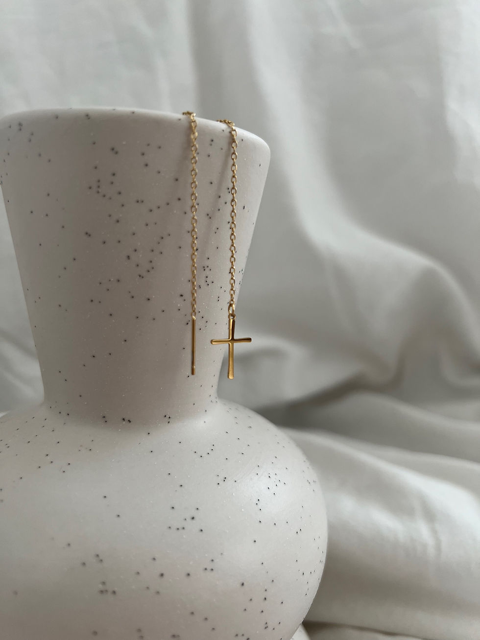 Goldene Ohrringe mit Kreuz-Anhänger an einer Vase, Detailaufnahme, nah, elegant.