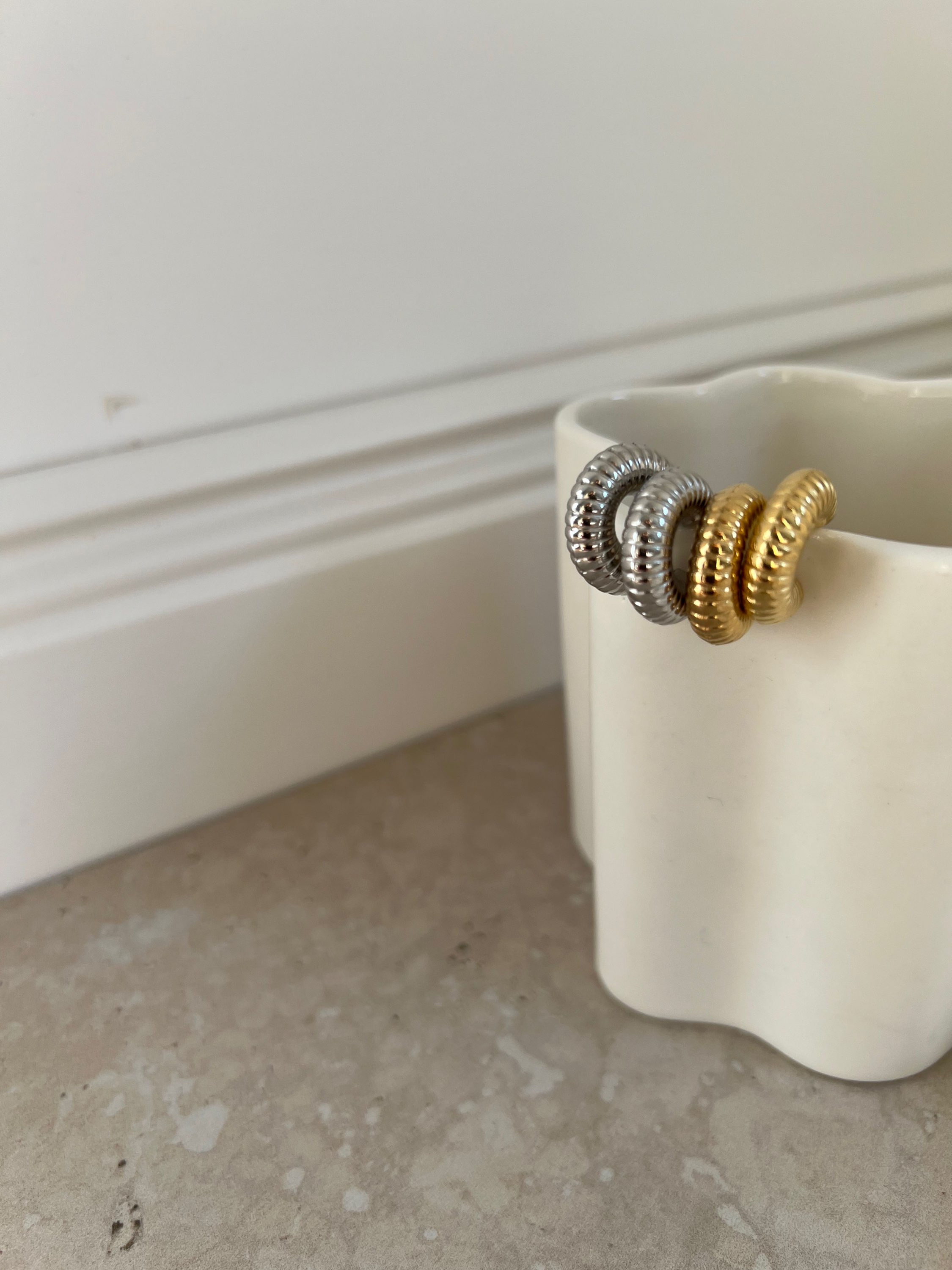 Drei goldene und silberne Ohrringe in einem weißen Becher liegen nah.