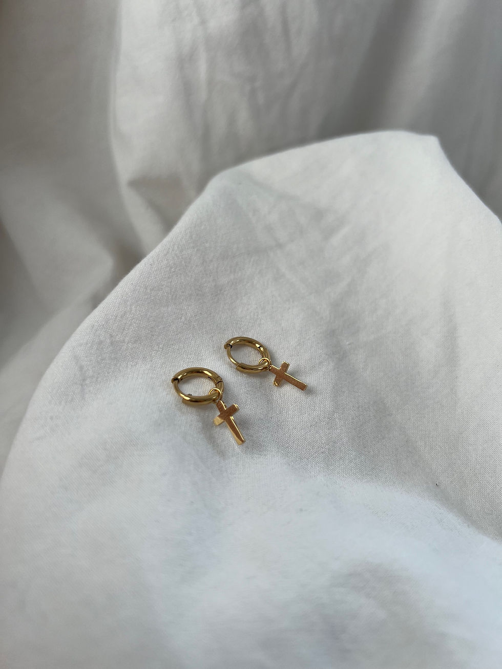 Goldene Ohrringe mit Kreuzanhänger auf weißem Stoff. Mein Schatz