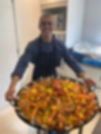 Chef Quint segurando a paelleira com paella pronta durante evento gastronômico em Florianópolis, representando a culinária autoral e ingredientes frescos da ilha.