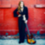 Keylab teacher, Lucy Clifford, posing against a brick wall with her bass guitar.