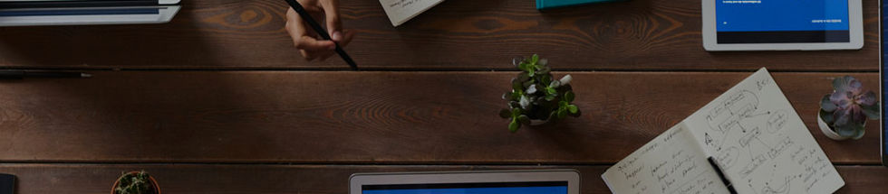 a shot from above of several hands, laptops, and pads of paper on a table as if gathered for a meeting