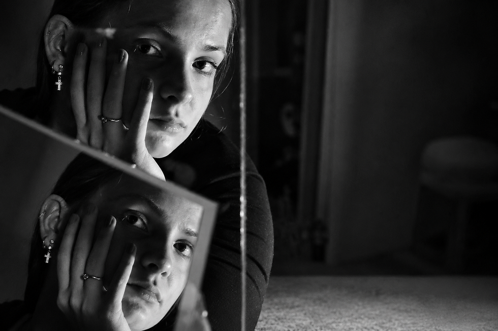 Pessoa observando o próprio reflexo em um espelho, em imagem em preto e branco, representando autoimagem, identidade e reflexão sobre si mesma.