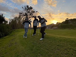 Drei junge Golfer bei Sonnenuntergang auf einem grünen Hügel