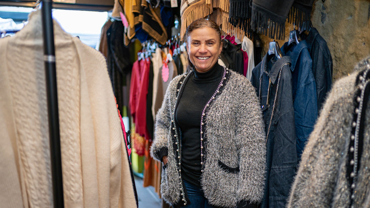 Woman smiles, surrounded by clothing racks, inside a shop, East Street Market.