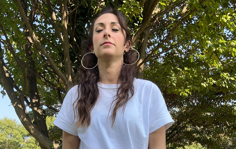 Sara Quieti, fondatrice di Onda Gipsy, un progetto che accompagna le donne a riconnettersi con cerchi, mentoring e retreat; l'immagine rappresenta Sara Quieti in primo piano che ha gli occhi chiusi seduta sul tappetino in mezzo alla natura, sta facendo dei respiri consapevoli per prendersi un momento di silenzio con sè stessa