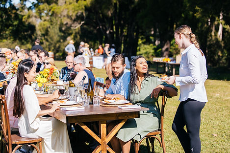 People of various ages dining outside around a wooden table