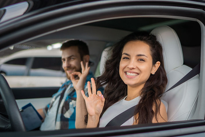 Happy woman and male instructor showing ok gesture while sitting in the car during drive t