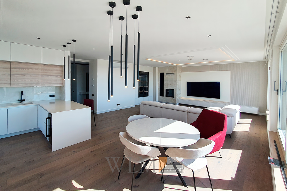 Просторная гостиная, выполненная в одном стиле с белоснежной кухней и акцентами из черного стекла в дверцах шкафов, l