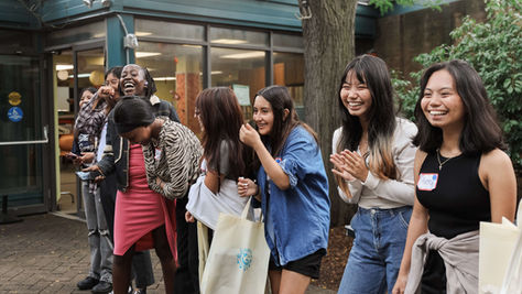 A group of smiling youth stand outside a building, holding tote bags, during the Summer Wellness Program in August 2024.