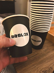 Hand holding a black paper cup with the Roblox logo.