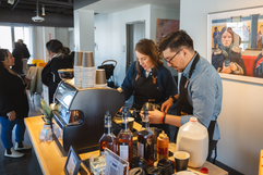 Two baristas prepare coffee drinks with an espresso machine in a cafe.