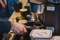 Barista fills espresso portafilter with ground coffee from commercial grinder, DANGER.