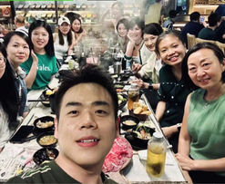 Group photo of people at restaurant table smiling, enjoying meal together.