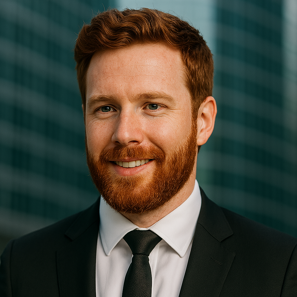 a portrait of a ginger haired gentleman smiling with a slight head tilt against a background of a blurred window.