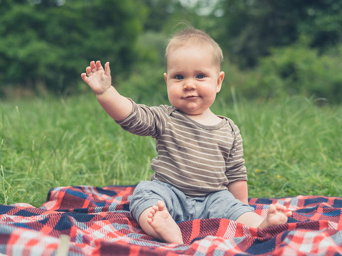 Baby sitting on blanket in grass waving