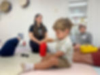 Child playing with Instruments in Mi Casa Es Tu Casa Class, Parents seen in background connecting.
