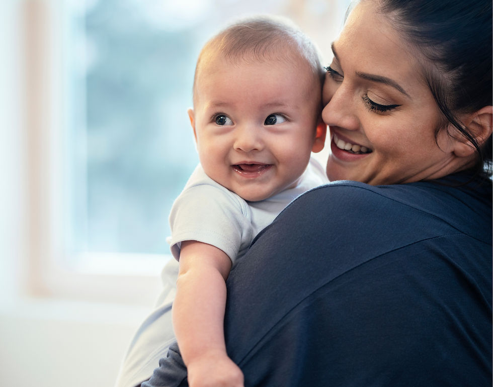 Smiling baby in the arms of a smiling mom in a sunny room