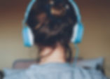 A picture of the back of a person's head. The person is wearing blue wired headphones