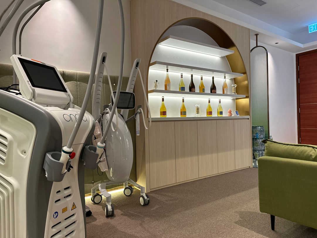 High-tech aesthetic machines next to a backlit skincare product display shelf in a modern beauty clinic.