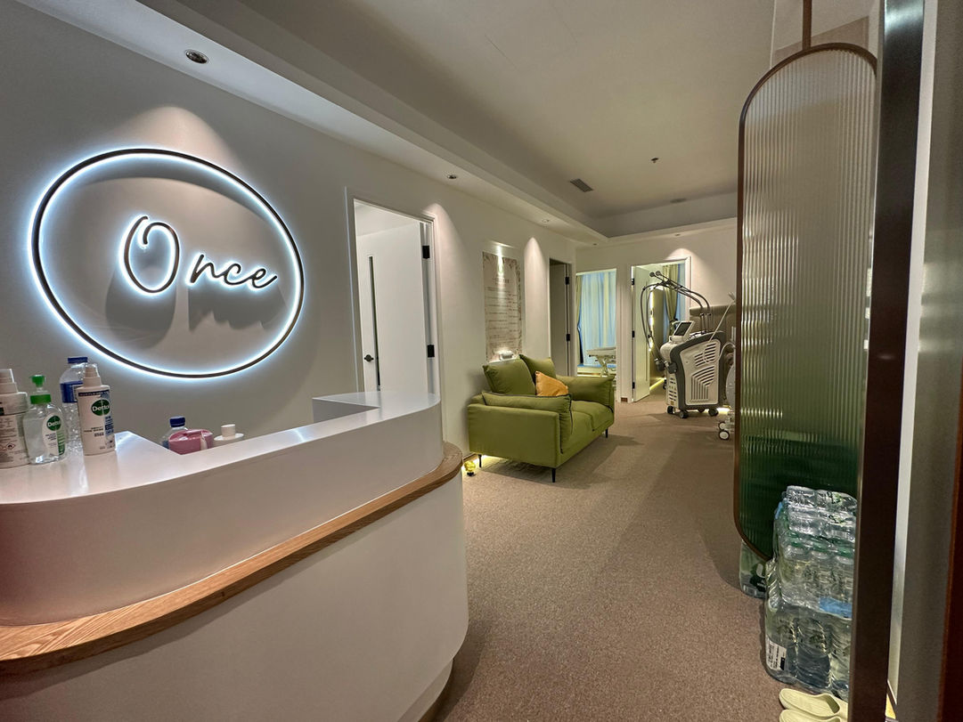 Reception area of Once Aesthetic Clinic with neon logo and comfortable green chairs