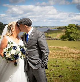 Bride and groom sharing a kiss at Blackton Grange, surrounded by countryside views and Balderhead Reservoir in the background on their wedding day.