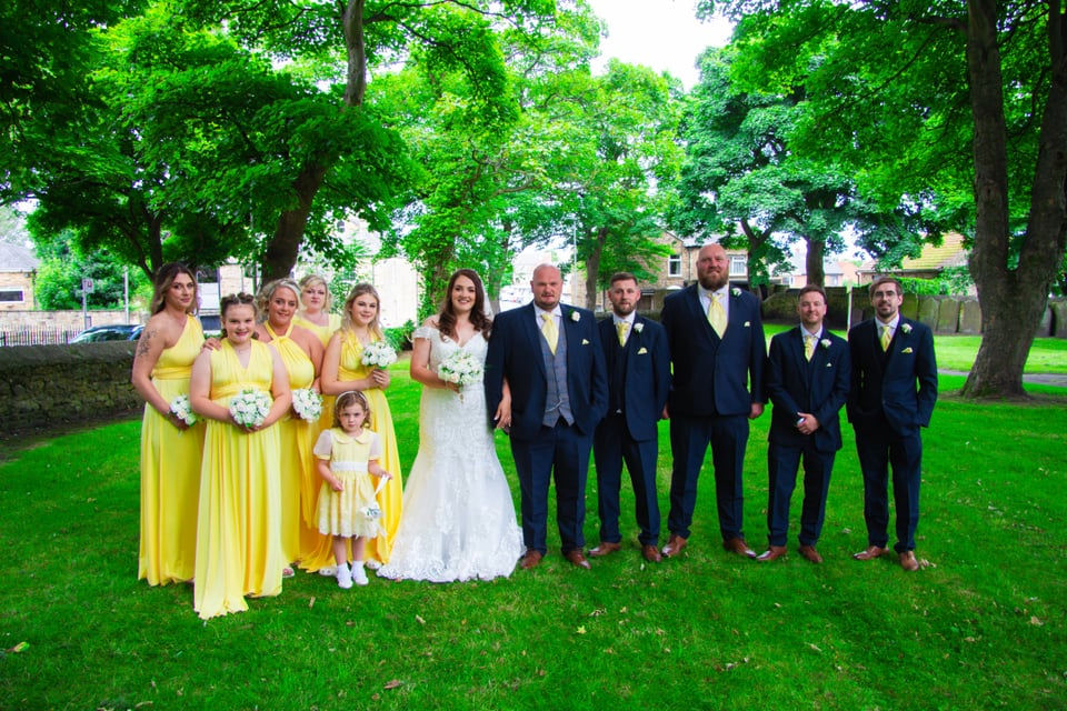 Wedding group photo outdoors with bride, groom and bridal party on grass in UK wedding venue