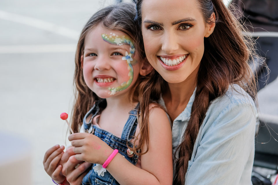 A children's ministry worker posing with one of the children who's face was just painted at a face painting booth during a children's event