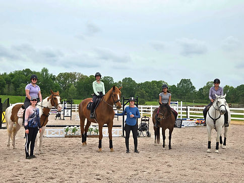 Group of riders on horses with an instructor in an outdoor arena.