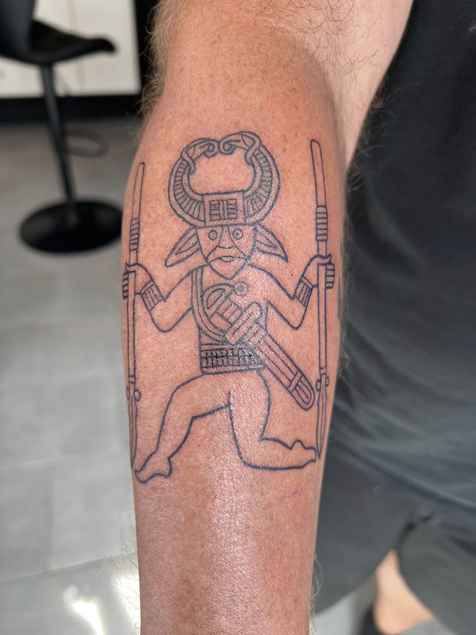 Fine-line black figure tattoo titled Woden on the lower leg