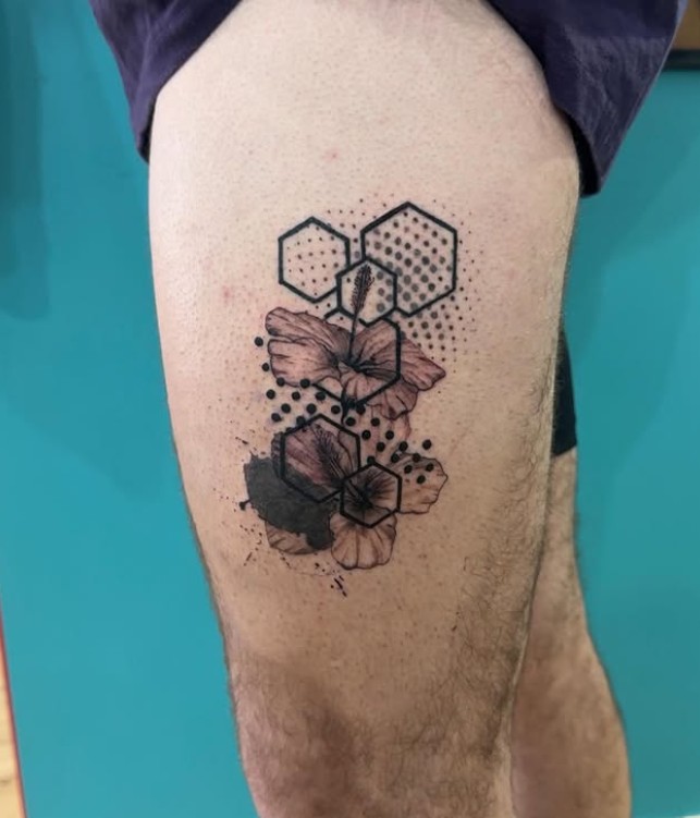 Black-and-grey geometric floral tattoo with hexagons and stippled dots on the upper leg