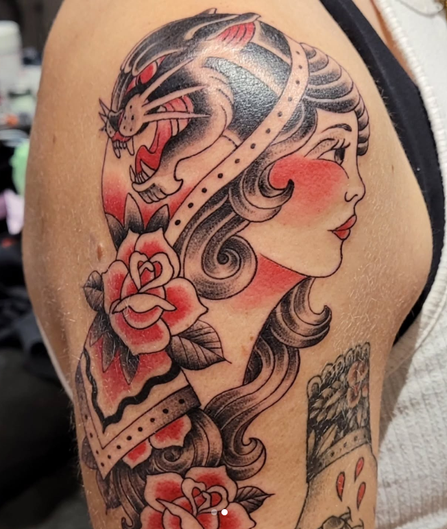 Vivid red-and-black lady-face tattoo with a panther head and roses on the upper arm