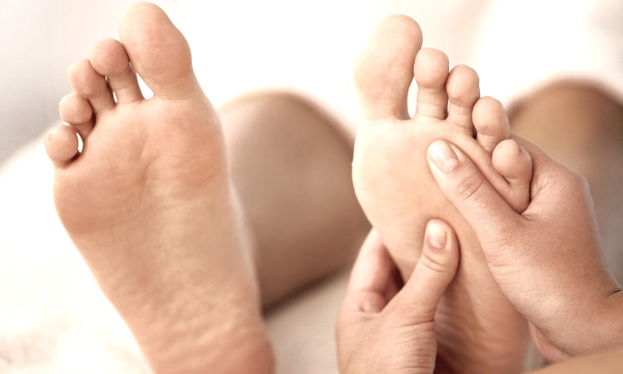 Mains de la thérapeute touchant délicatement les deux pieds lors d’une séance de réflexologie.