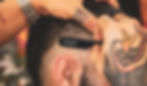 A barber with tattooed hands cutting a mans hair using a black razor with the Stems Barbershop logo