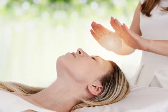 Kvinde ligger på briksen og modtager healing fra behandlerens varme hænder.Healing og fjernhealing. Slip spændinger i krop, sind og sjæl med healing - også fjernhealing